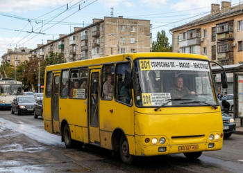 типичный желтый одесский автобус «Богдан» №201, застывший в заторе на одной из улиц города. Кабина водителя украшена деталями, которые сразу узнает любой одессит — например, герб города, флажок Украины и винтажные часы. На лобовом стекле четко видна табличка с номером «201» и маршрутом: «СТАРОСЕННАЯ ПЛ. — Ж/Д ВОКЗАЛ — ЛЕНПОСЕЛОК